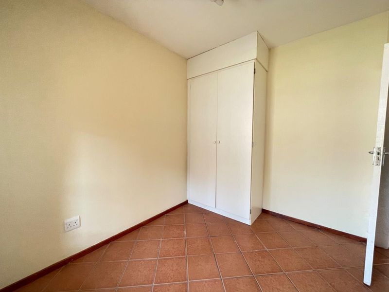 A simple, empty bedroom featuring tiled flooring and a built-in white wardrobe, offering a clean and neutral space ready for personalization.
