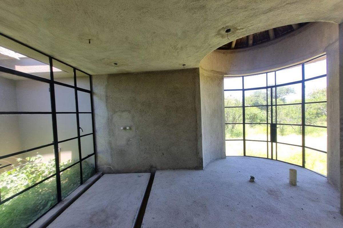 An unfinished interior space featuring large black-framed steel windows, exposed concrete flooring, and raw plaster walls, offering a blank canvas for custom finishes.