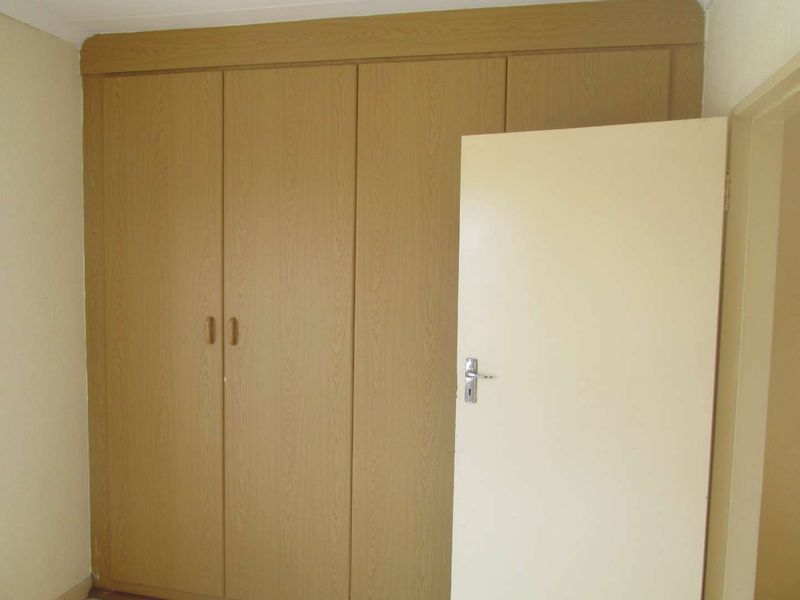A bedroom interior featuring built-in wooden cupboards and a standard internal door.