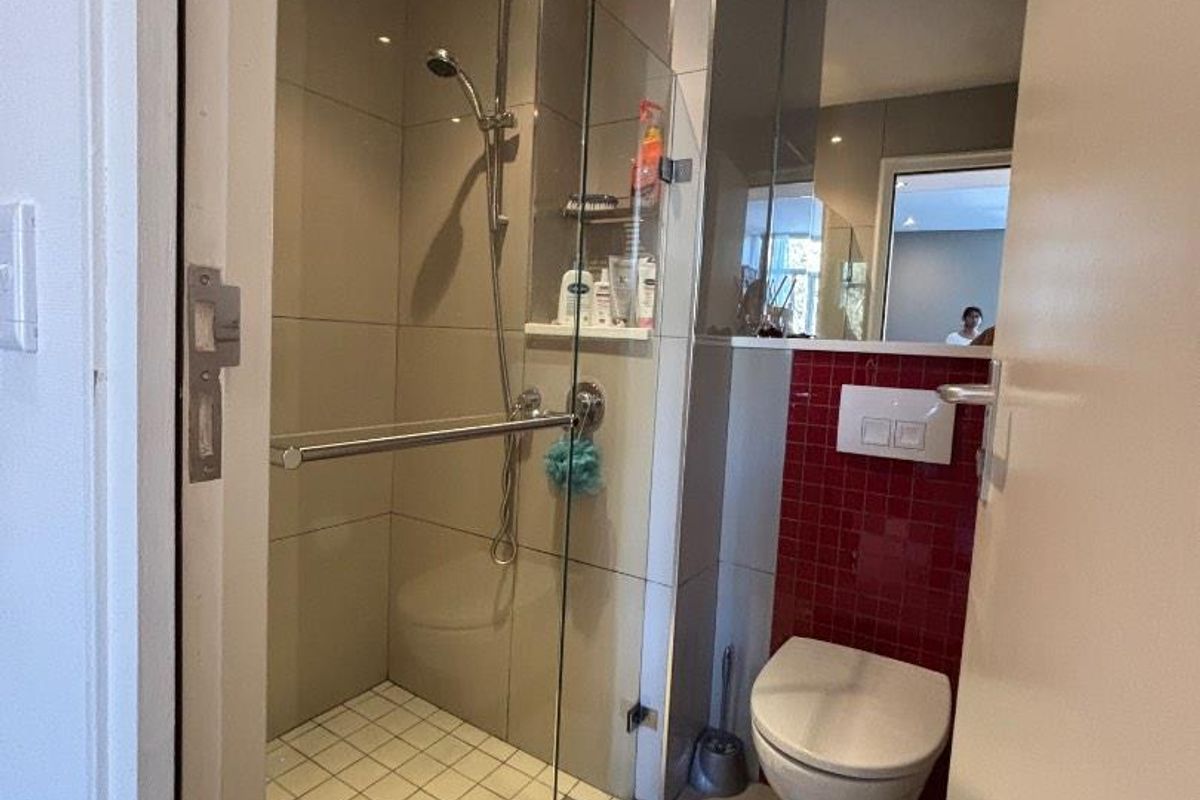 Compact modern bathroom featuring a glass-enclosed shower, wall-mounted toilet, and a striking red mosaic tile accent wall.