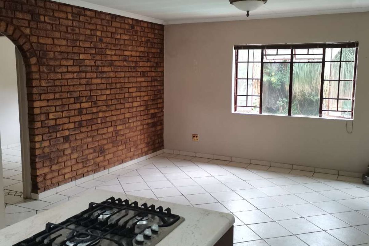 Spacious kitchen area featuring a built-in gas hob, tiled flooring, and a distinctive exposed brick feature wall with an arched entryway.