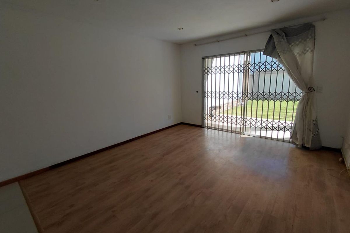 An empty living room featuring laminate flooring, recessed lighting, and a sliding glass door with a security gate leading to the exterior.