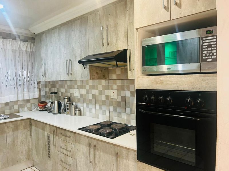 A functional kitchen featuring modern wood-look cabinetry, a built-in oven, hob, extractor fan, and a tiled backsplash with stone countertops.