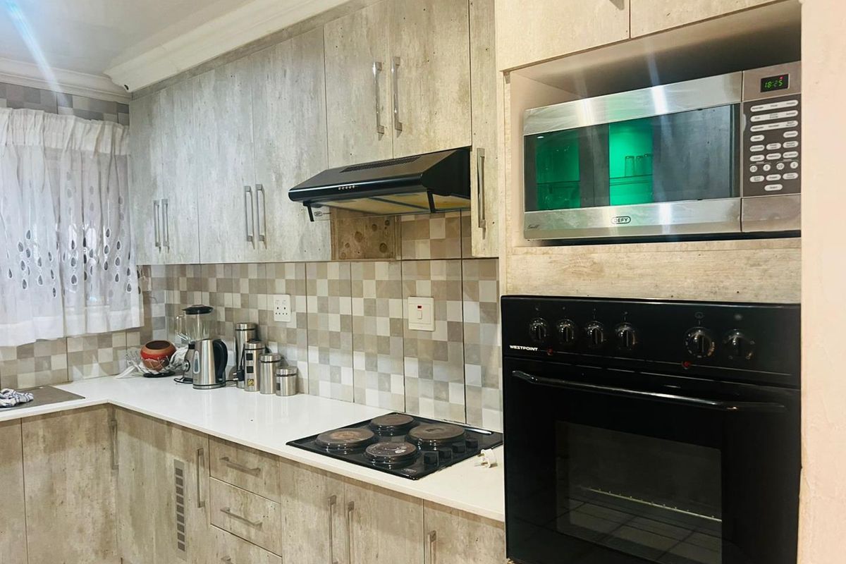 A functional kitchen featuring modern wood-look cabinetry, a built-in oven, hob, extractor fan, and a tiled backsplash with stone countertops.