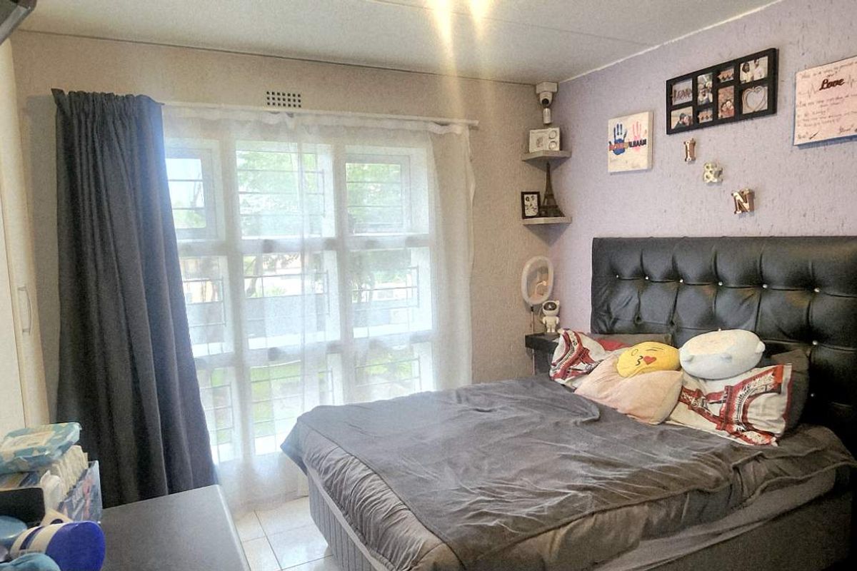 A bedroom featuring built-in cupboards, tiled flooring, and a window with security bars, providing a functional living space.
