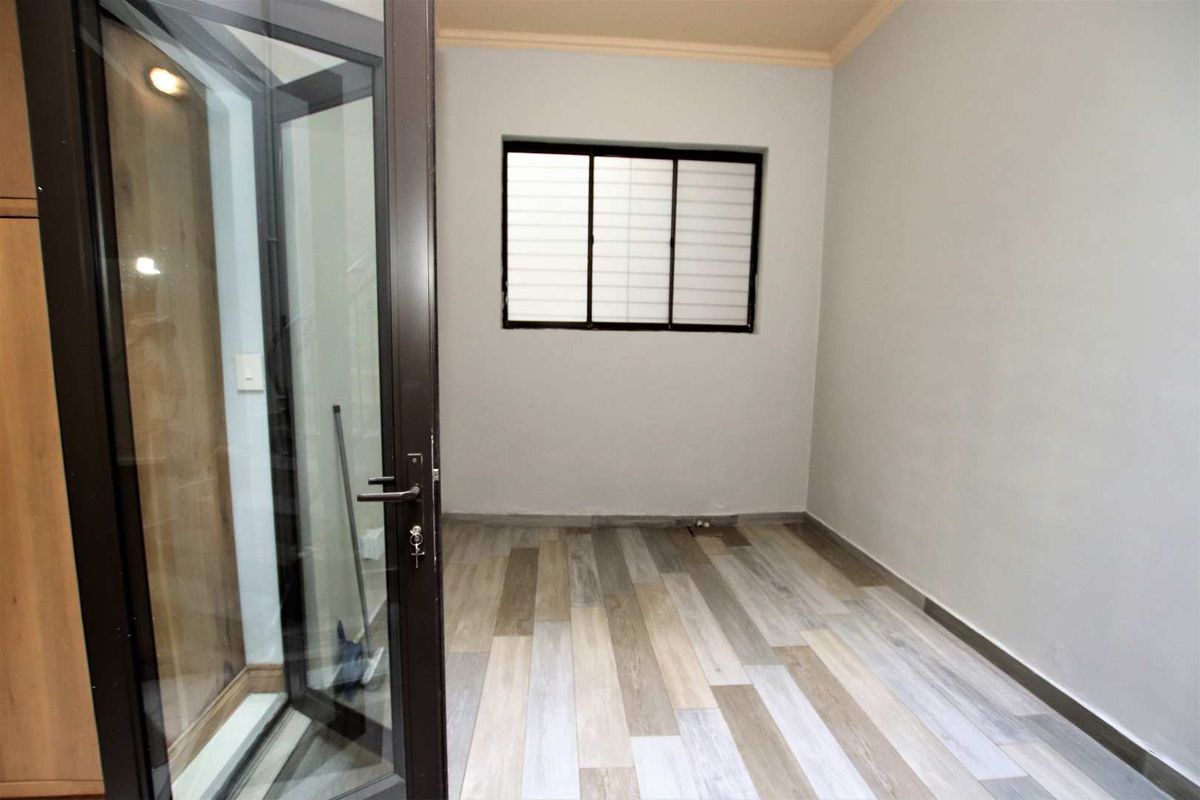 A clean, empty room featuring wood-look tile flooring, a window with security bars, and a glass-paneled door leading to an adjacent space.
