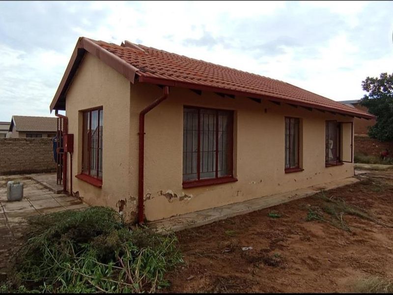 Rear view of a detached house featuring terracotta roof tiles, burglar bars, and a paved patio area with visible exterior wall maintenance required.