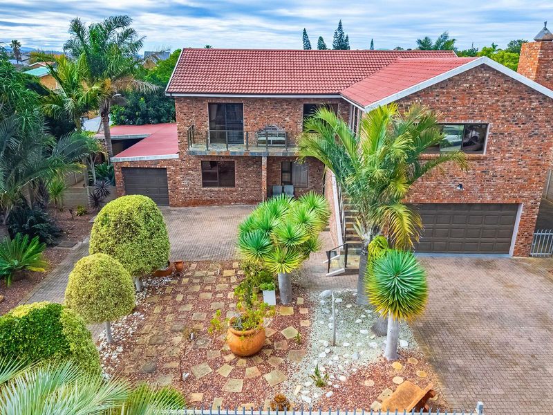 Aerial view of a double-story brick house featuring a tiled roof, paved driveway, double garage, and an upper-level balcony.