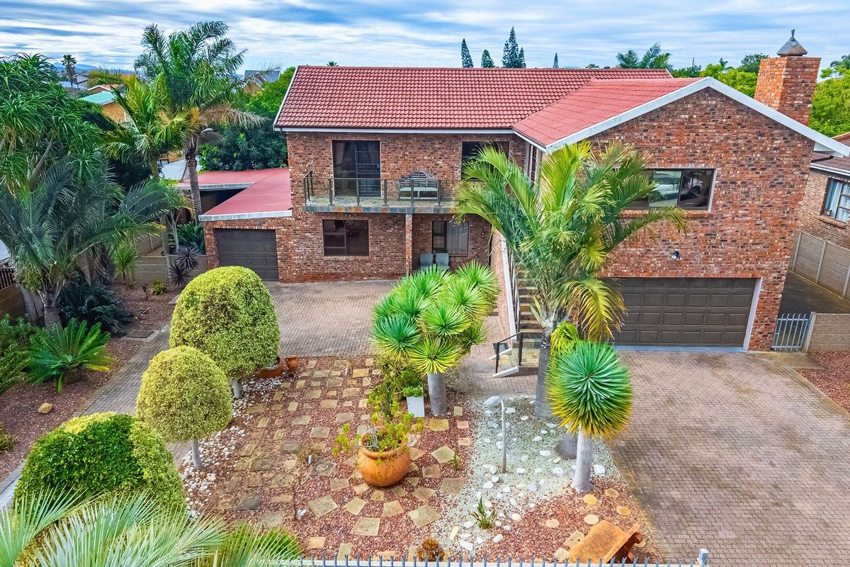 Aerial view of a double-story brick house featuring a tiled roof, paved driveway, double garage, and an upper-level balcony.