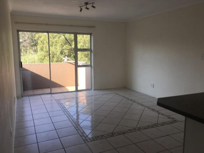 An empty open-plan living area featuring tiled flooring with a decorative border, a breakfast bar, and a sliding door leading to a balcony.