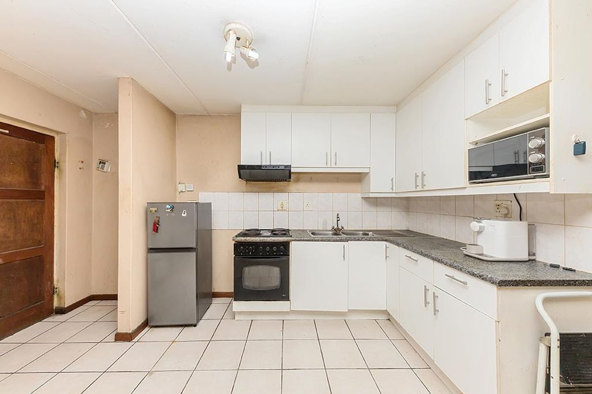 A functional kitchen featuring white cabinetry, laminate countertops, a built-in stove with extractor fan, and tiled flooring, offering potential for modernization.