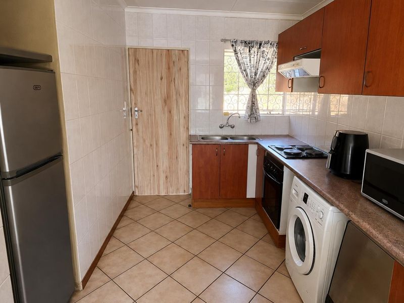 Functional kitchen featuring wood-finish cabinetry, tiled splashbacks, integrated oven and hob, and dedicated space for laundry appliances.