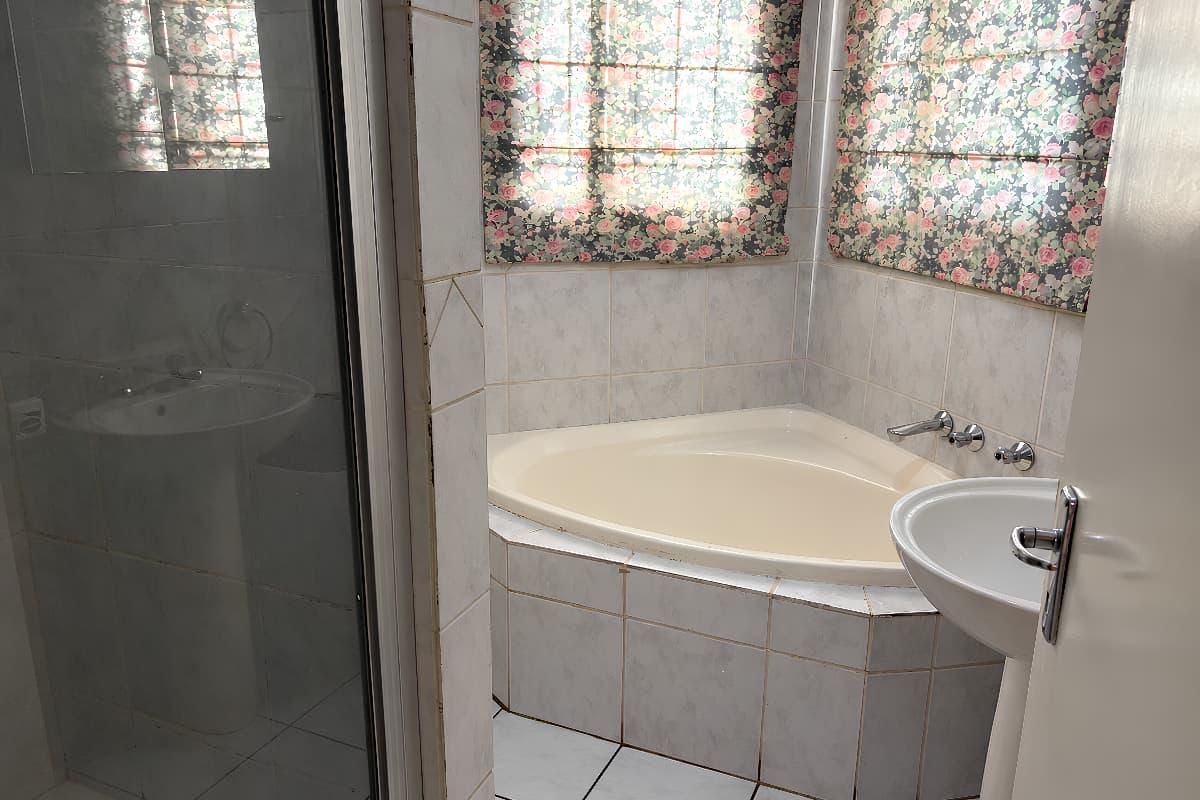 A dated bathroom featuring a corner bathtub, pedestal sink, and a separate shower enclosure with tiled surfaces throughout.