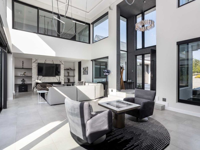 Spacious double-volume living room featuring a striking marble fireplace, extensive built-in shelving, and large floor-to-ceiling windows that provide abundant natural light.