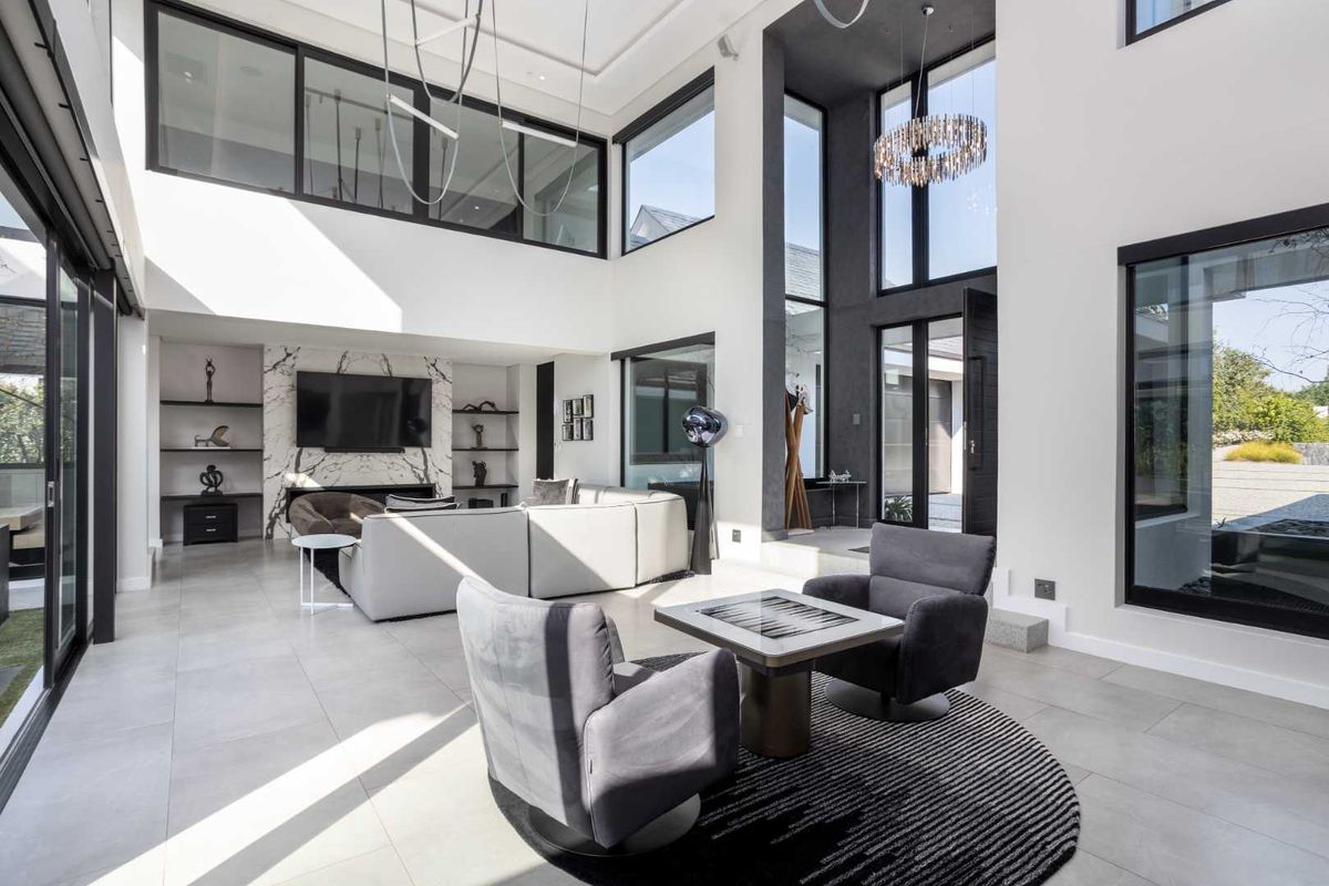 Spacious double-volume living room featuring a striking marble fireplace, extensive built-in shelving, and large floor-to-ceiling windows that provide abundant natural light.