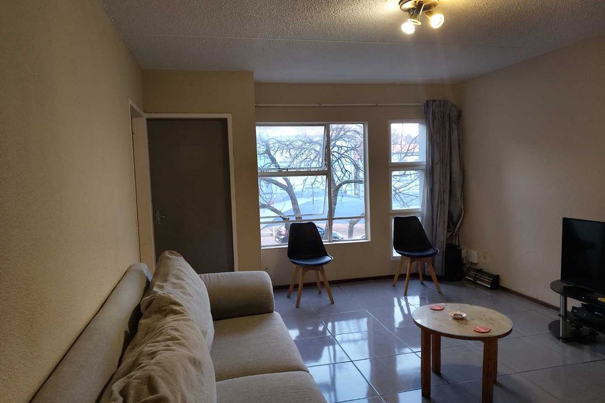 A living room featuring tiled flooring and large windows, providing a functional space with potential for modern updates to enhance its overall appeal.