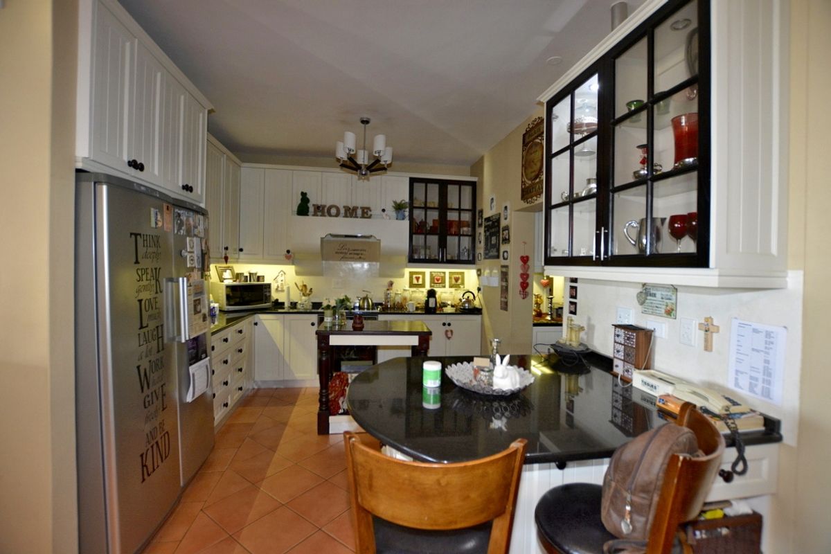 A functional kitchen featuring white cabinetry, dark granite countertops, a central island, and tiled flooring with integrated storage and display cabinets.