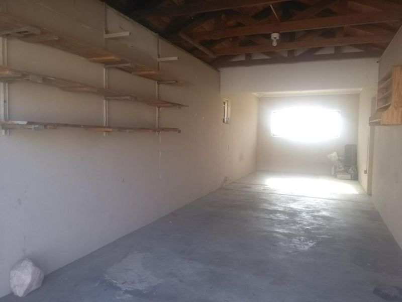 A spacious, empty garage featuring exposed timber roof trusses, concrete flooring, and wall-mounted shelving, offering versatile storage or workshop potential.