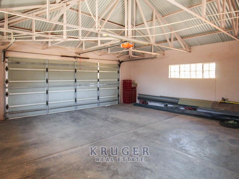 A spacious, empty garage featuring exposed roof trusses, a sectional garage door, and durable concrete flooring.