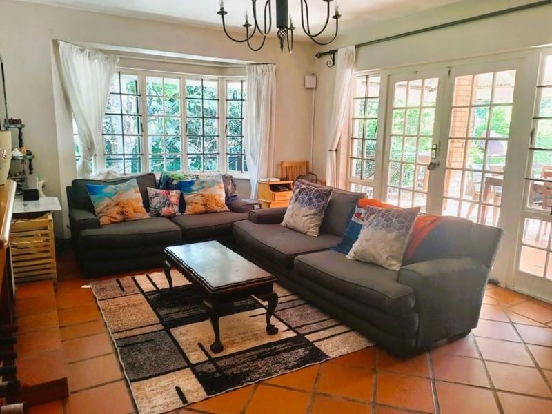 A bright living room featuring terracotta floor tiles, a large bay window, and double french doors providing access to the outdoor patio area.