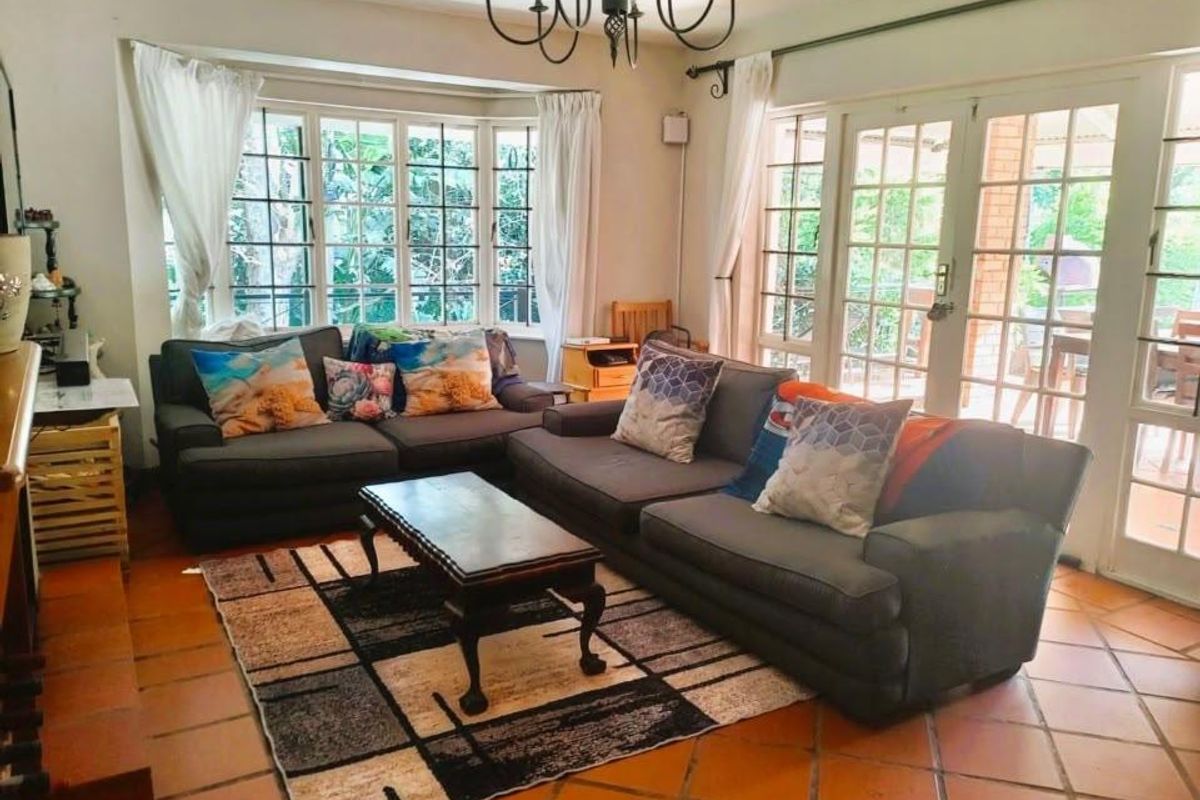 A bright living room featuring terracotta floor tiles, a large bay window, and double french doors providing access to the outdoor patio area.
