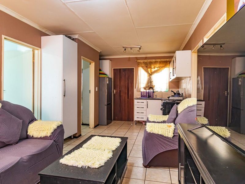 Open-plan living and kitchen area featuring tiled flooring, built-in cabinetry, and a large wall mirror, offering a functional layout with potential for modernization.