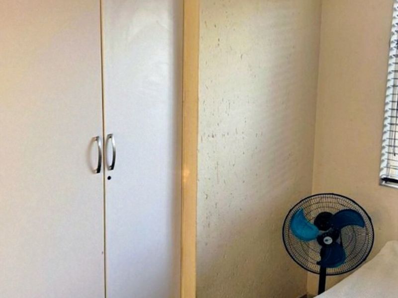 A bedroom featuring a built-in wardrobe, tiled flooring, and a window with blinds. The walls show visible signs of wear and surface damage.