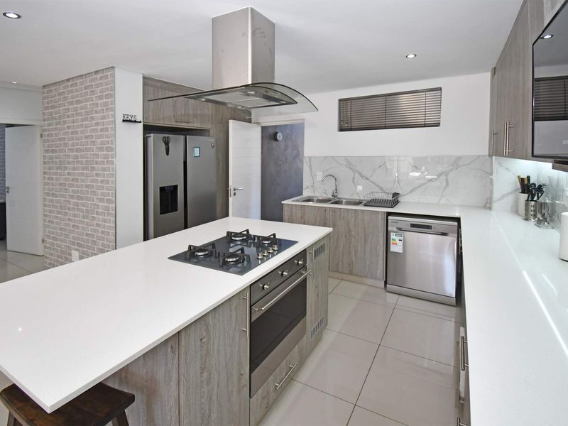 Modern kitchen featuring a central island with gas hob, built-in oven, sleek quartz countertops, marble-look splashback, and high-quality cabinetry.