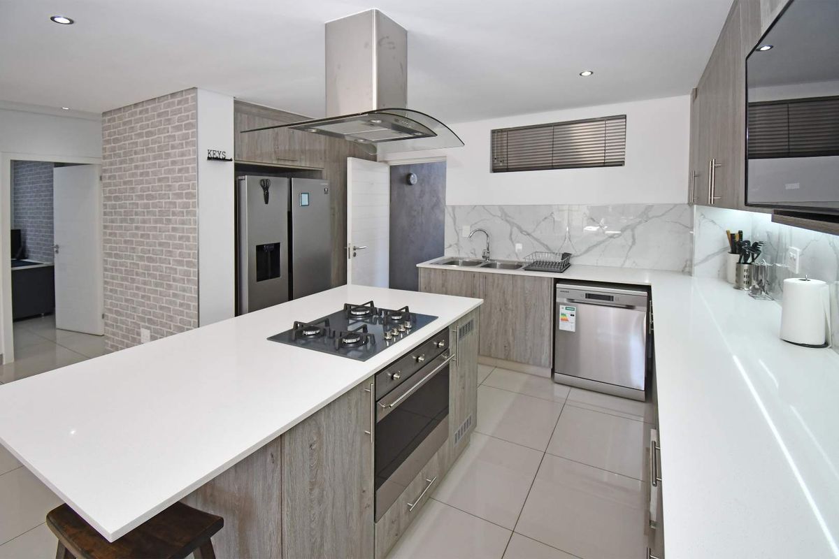 Modern kitchen featuring a central island with gas hob, built-in oven, sleek quartz countertops, marble-look splashback, and high-quality cabinetry.