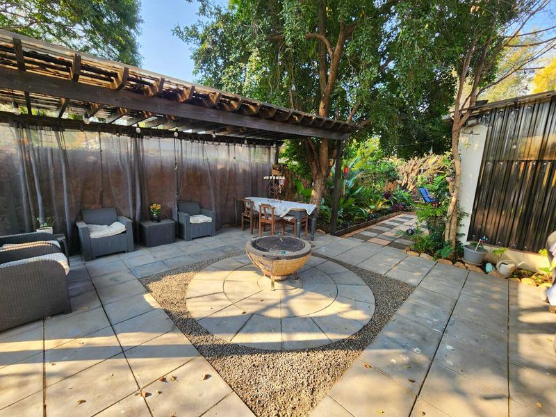 Outdoor patio area featuring a timber pergola, paved flooring with a central fire pit, and established garden surroundings.