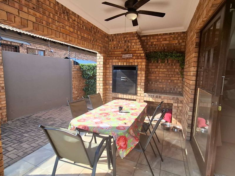 Covered patio area featuring exposed brickwork, a built-in braai, and a ceiling fan, providing a functional space for outdoor dining and entertainment.
