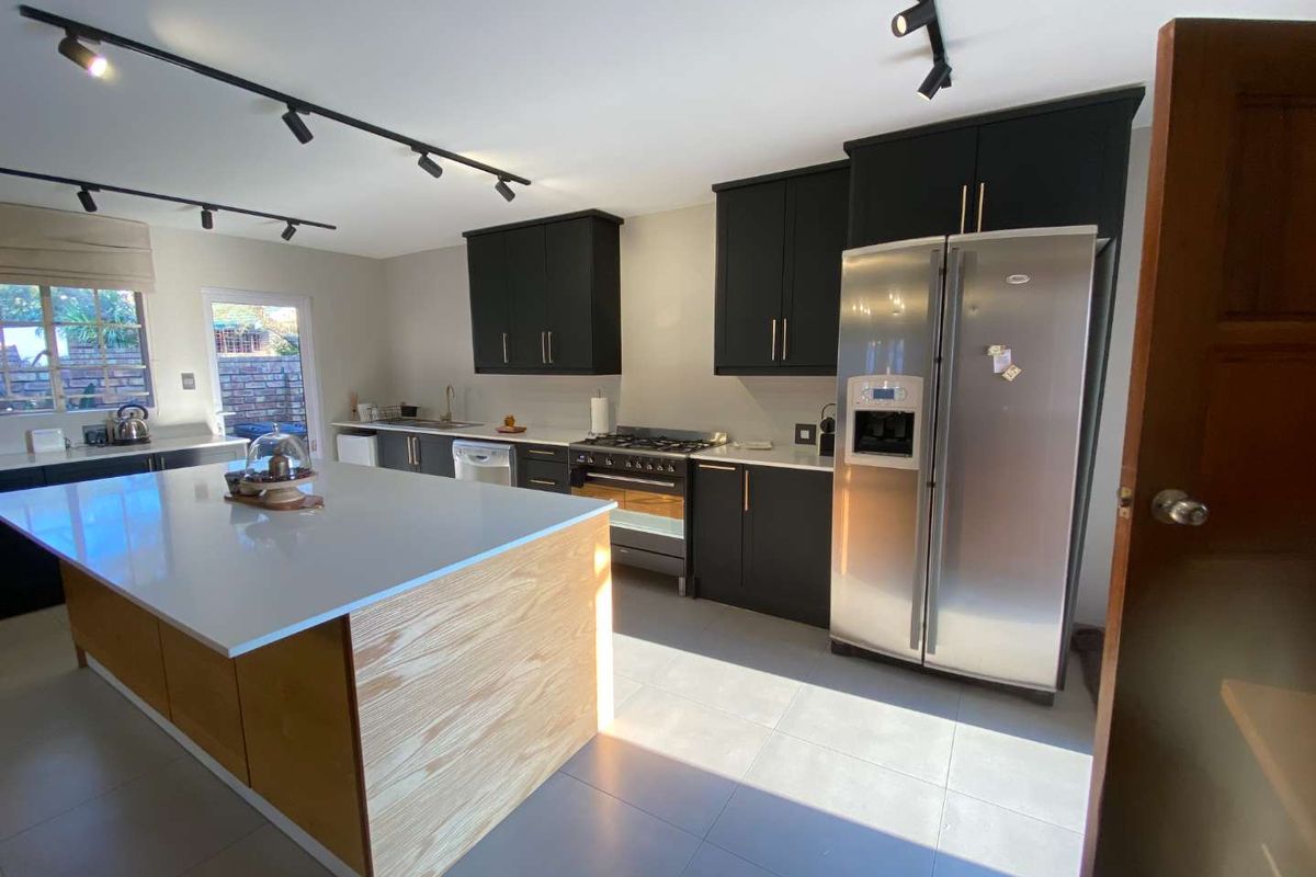 Modern kitchen featuring a large central island with quartz countertops, dark cabinetry, gas stove, and contemporary track lighting, offering a functional and stylish workspace.
