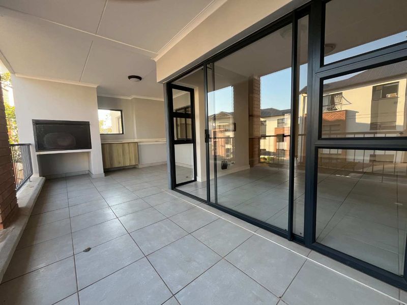 Spacious covered balcony featuring tiled flooring, a built-in braai, and modern sliding glass doors providing seamless access to the interior living area.