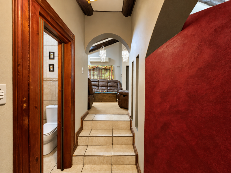 A tiled hallway featuring an arched entryway, exposed timber ceiling beams, and a striking red textured feature wall leading to the living area.