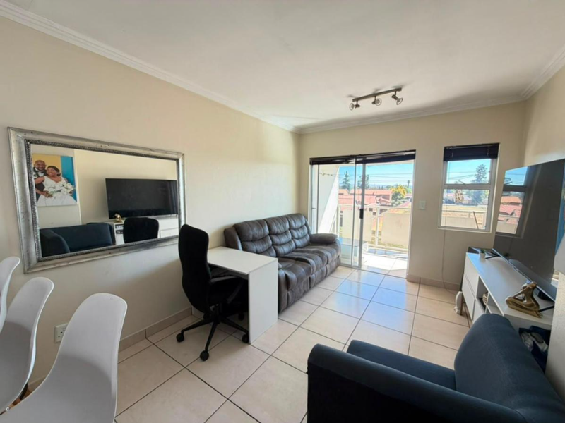 A bright living room featuring tiled flooring, coved ceilings, and a sliding glass door providing access to an outdoor balcony area.