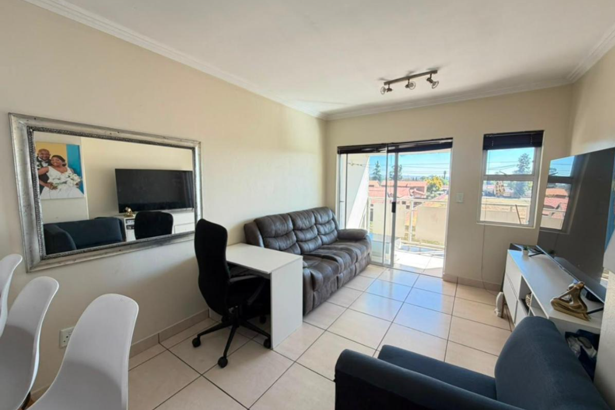 A bright living room featuring tiled flooring, coved ceilings, and a sliding glass door providing access to an outdoor balcony area.