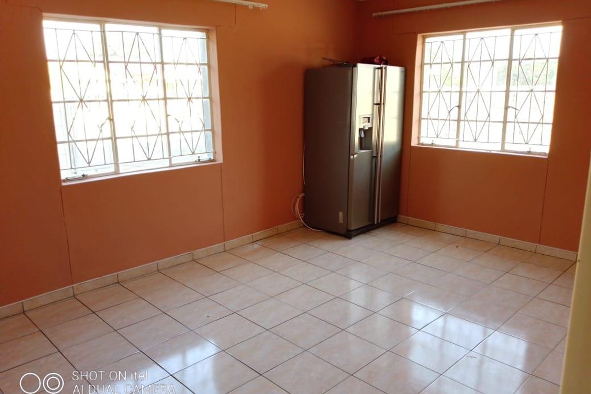 A spacious, empty living area featuring tiled flooring, large windows with security bars, and neutral wall finishes.