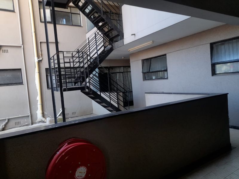 Exterior view of an apartment building rear courtyard featuring a metal fire escape staircase, fire hose reel, and balcony access.
