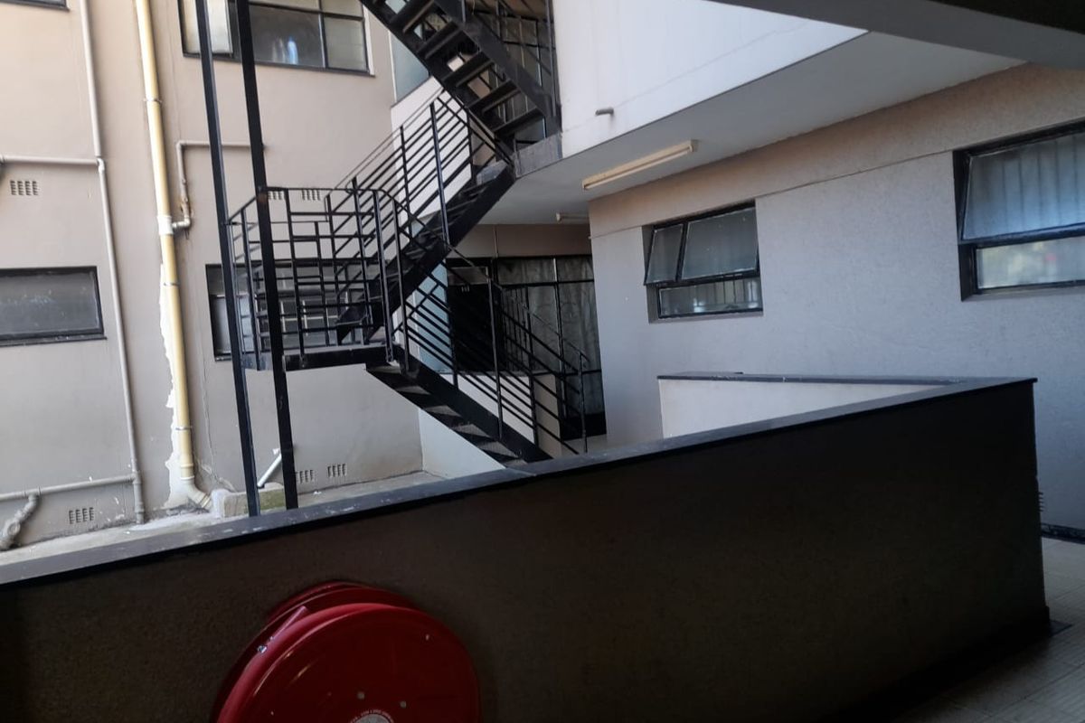 Exterior view of an apartment building rear courtyard featuring a metal fire escape staircase, fire hose reel, and balcony access.
