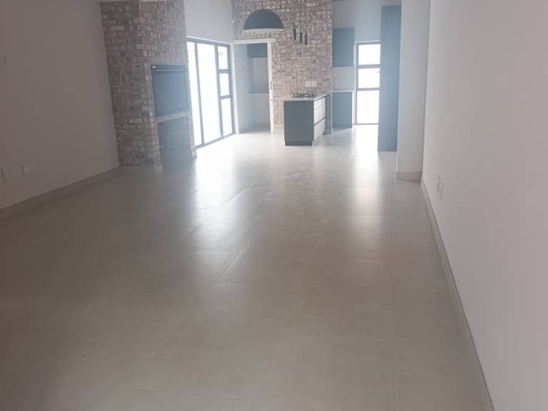 Spacious open-plan living and kitchen area featuring modern tiled floors, an exposed brick feature wall with a built-in fireplace, and a central kitchen island.