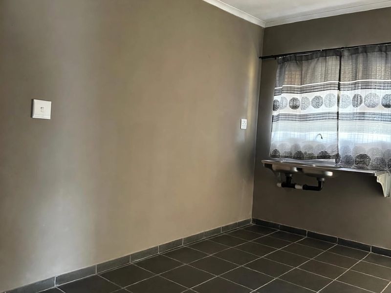 A functional laundry area featuring dark tiled flooring and a wall-mounted stainless steel sink.