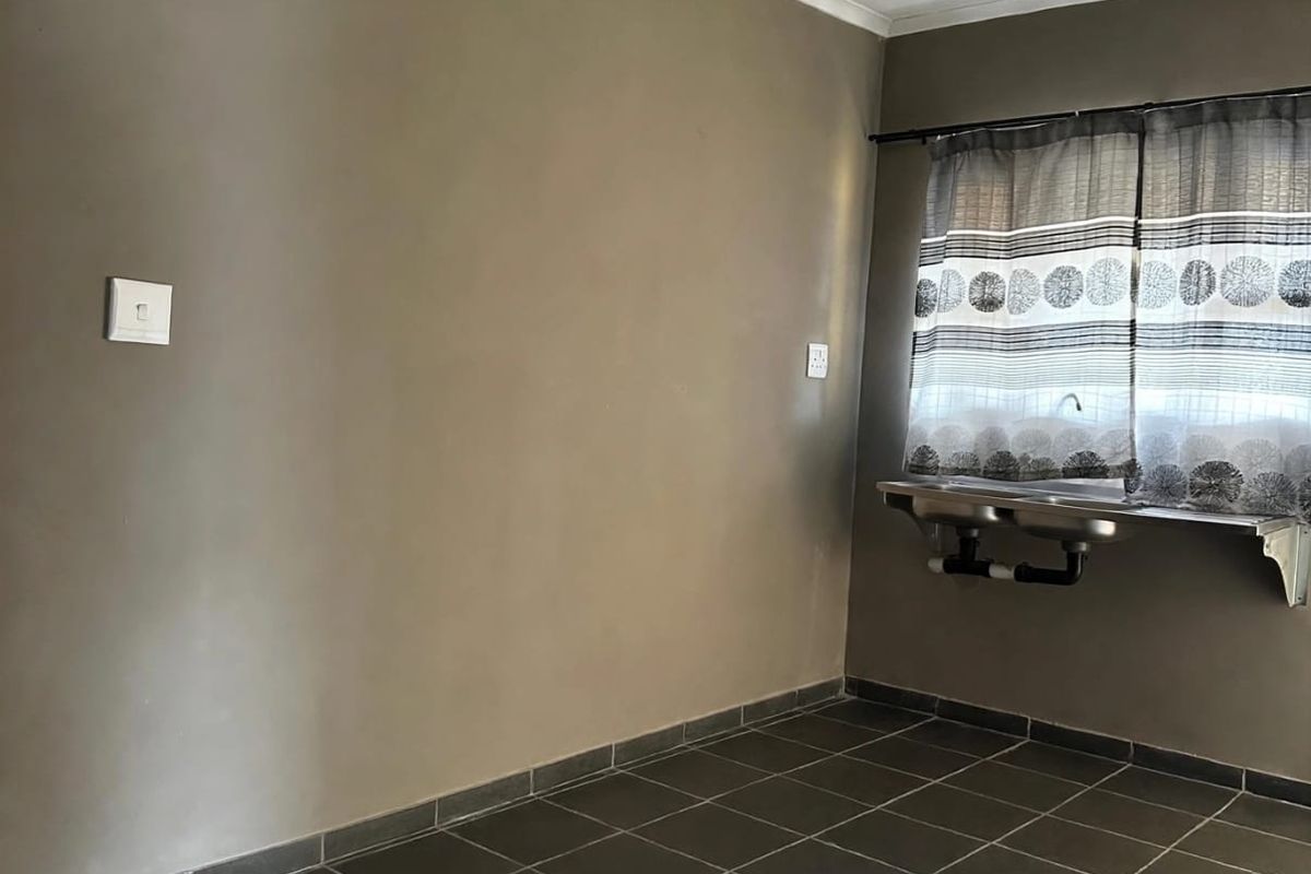 A functional laundry area featuring dark tiled flooring and a wall-mounted stainless steel sink.