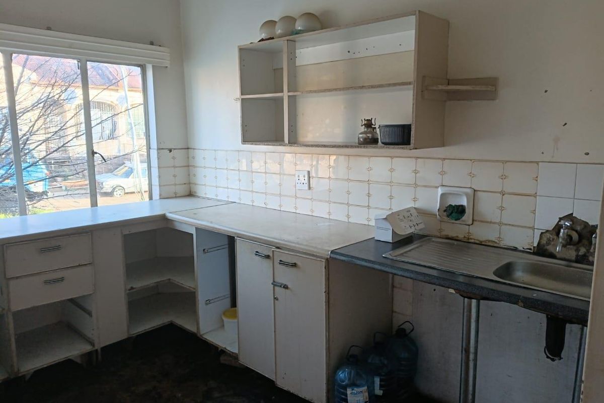A dated kitchen featuring original cabinetry, a stainless steel sink, and tiled splashbacks, requiring significant renovation and modernization.
