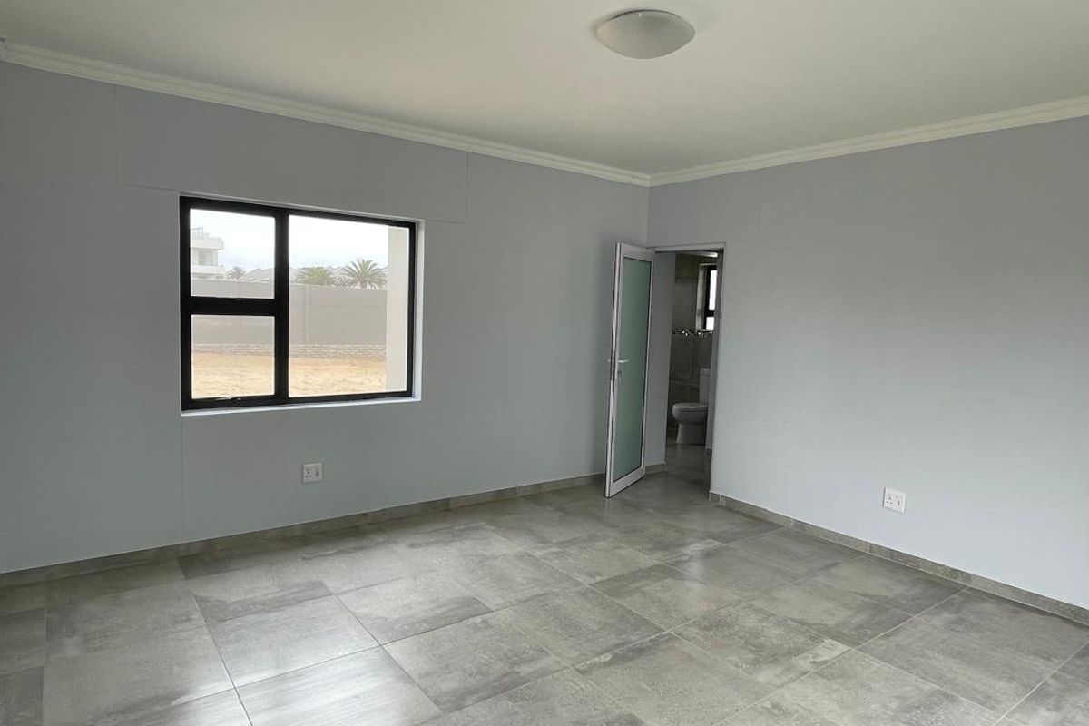 A bright, empty bedroom featuring large format grey floor tiles, neutral wall paint, and an en-suite bathroom access.