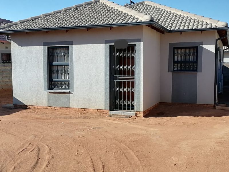 Front view of a single-story residential house featuring a tiled roof, security gate, and burglar bars, set on an unpaved plot.