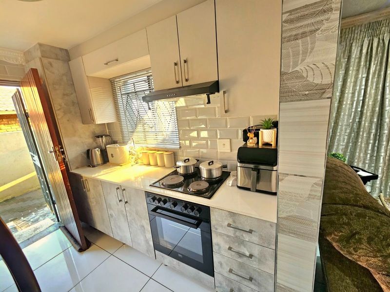 A modern kitchen featuring light-toned cabinetry, a subway tile backsplash, stone countertops, and integrated cooking appliances, with direct access to an outdoor area.