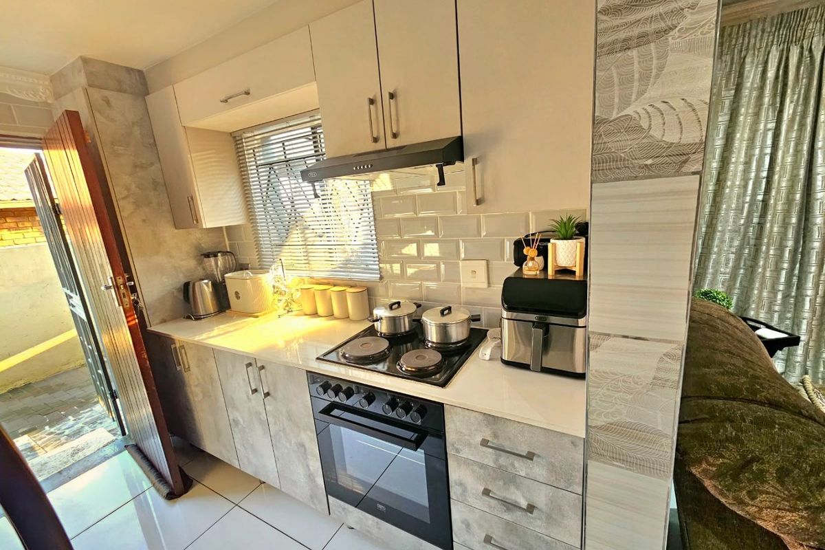 A modern kitchen featuring light-toned cabinetry, a subway tile backsplash, stone countertops, and integrated cooking appliances, with direct access to an outdoor area.