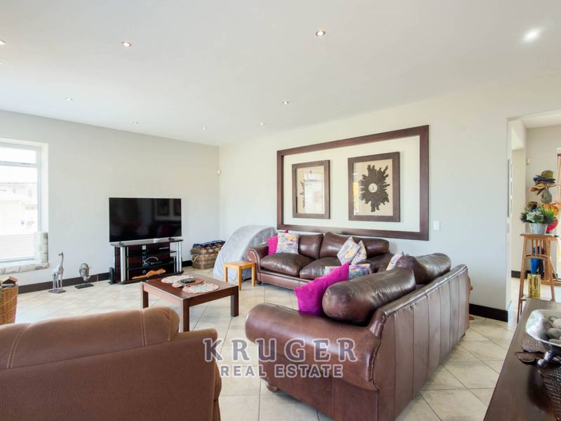 A spacious living room featuring neutral tiled flooring, recessed downlighting, and large windows that provide ample natural light.