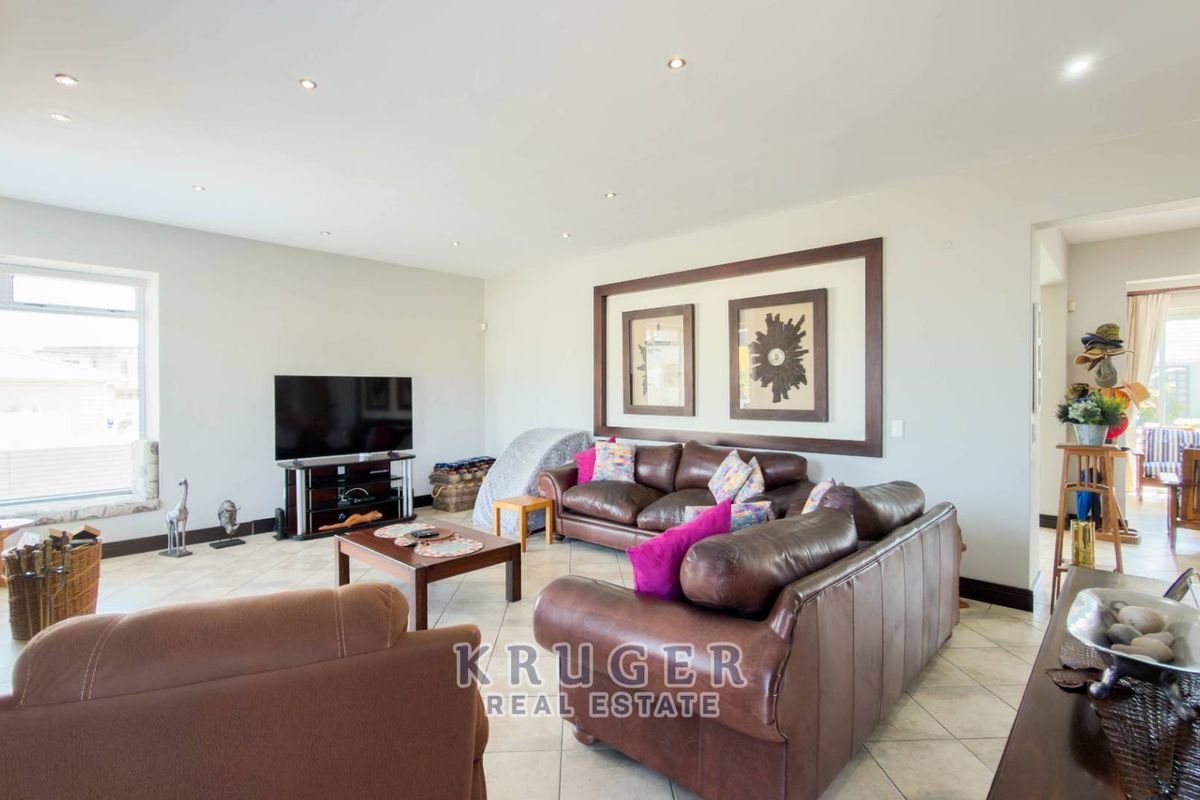 A spacious living room featuring neutral tiled flooring, recessed downlighting, and large windows that provide ample natural light.