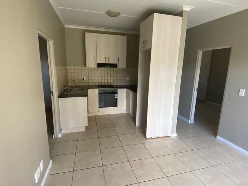 A functional kitchen featuring tiled flooring, built-in cabinetry, an integrated oven and hob, and a tiled backsplash, presented in a clean, empty state.